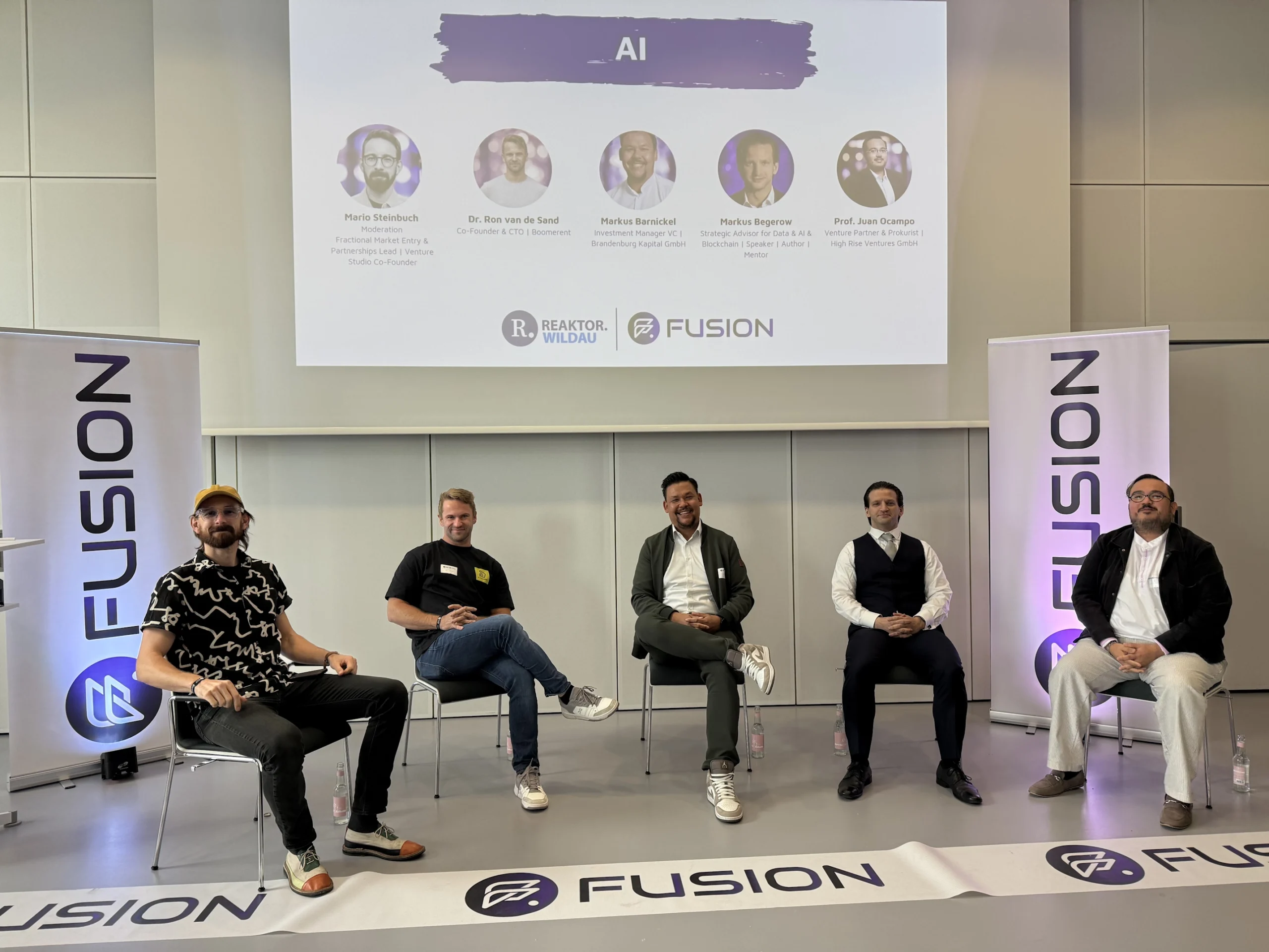Panelrunde zum Thema KI bei der FUSION 2026 im Reaktor Wildau mit fünf Teilnehmern vor der Veranstaltungsbühne.