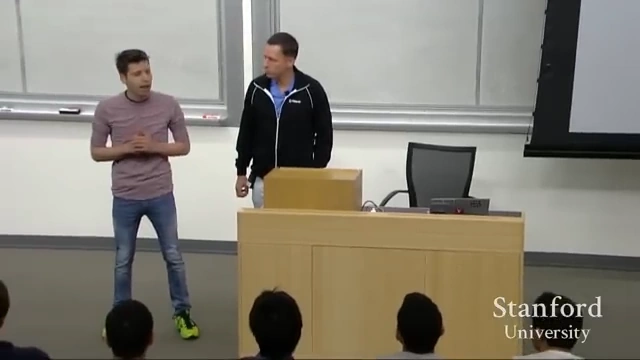 Sam Altman und Peter Thiel stehen während eines Vortrags an der Stanford University vor Studierenden auf einer Bühne und diskutieren über Unternehmertum, Innovation und Wettbewerb.